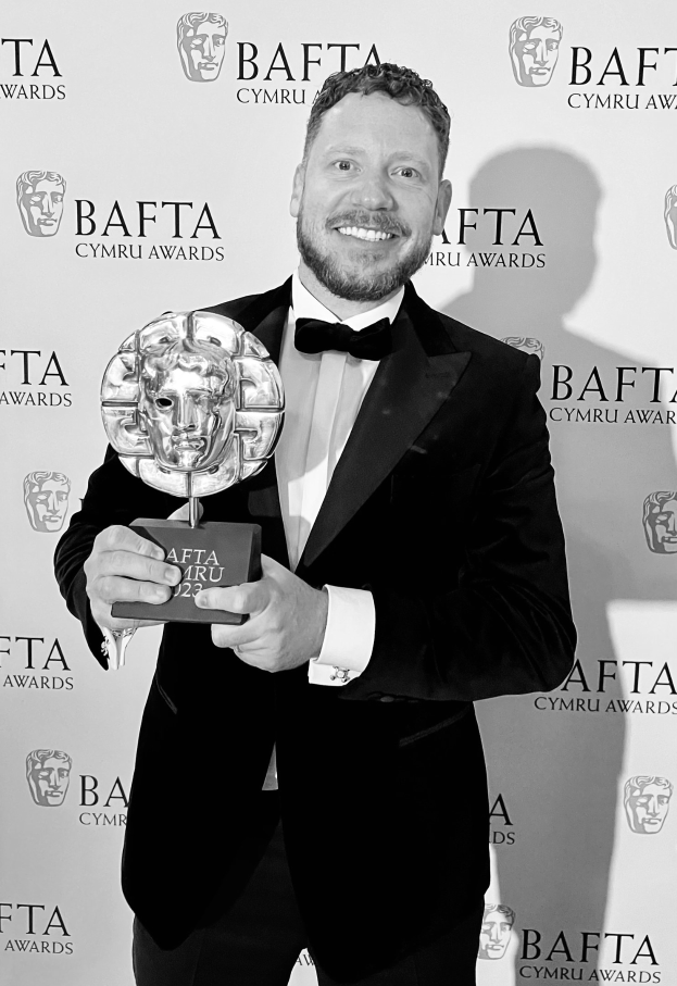 Ein Mann im Smoking, der eine BAFTA-Trophäe hält und vor einer Tafel mit "BAFTA Awards 2018" steht.