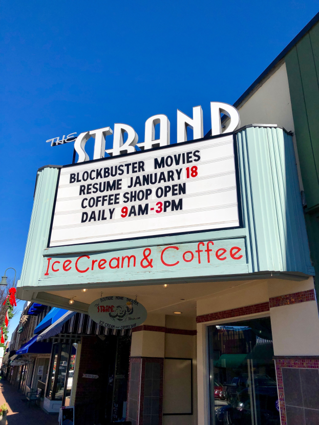 Die Strand-Blockbuster-Filme nehmen am 18. Januar wieder ihren Betrieb auf. Das Bild zeigt das Strand-Blockbuster-Kino, mit einem Namen auf dem Gebäude, einem Straßenschild, einer Gruppe von Bäumen, einigen Pflanzen in Töpfen und einem bewölkten Himmel.