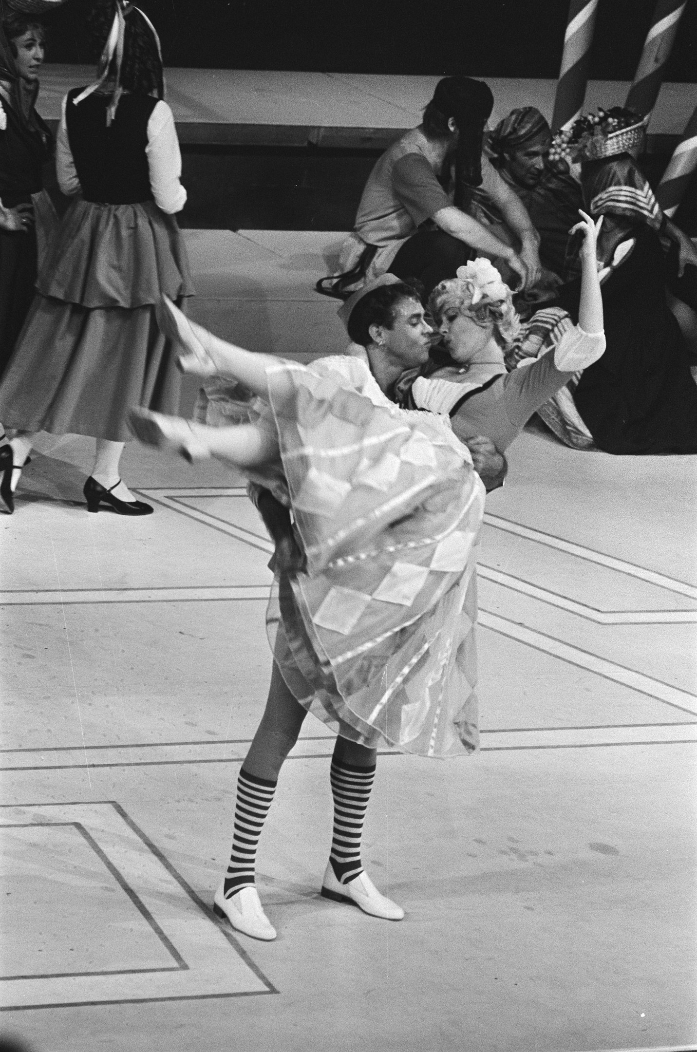 Schwarzes und weißes Foto von zwei Menschen, die auf einer Bühne tanzen, mit einigen Zuschauern auf einer Treppe im Hintergrund und einem Pfahl im Vordergrund.