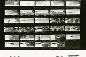 Schwarzes und weißes Foto eines Mannes in einem weißen Hemd und Shorts, der konzentriert Tennis spielt und einen Schläger in der rechten Hand hält, vor einem Filmstreifen-Hintergrund.