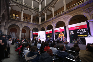 Eine Gruppe von Menschen, die an einem Tisch mit einem Podium und einem Mikrofon vor einer Menge, Kameras und Bannern sitzen, während einer Pressekonferenz für das CDMX 2017-Event.