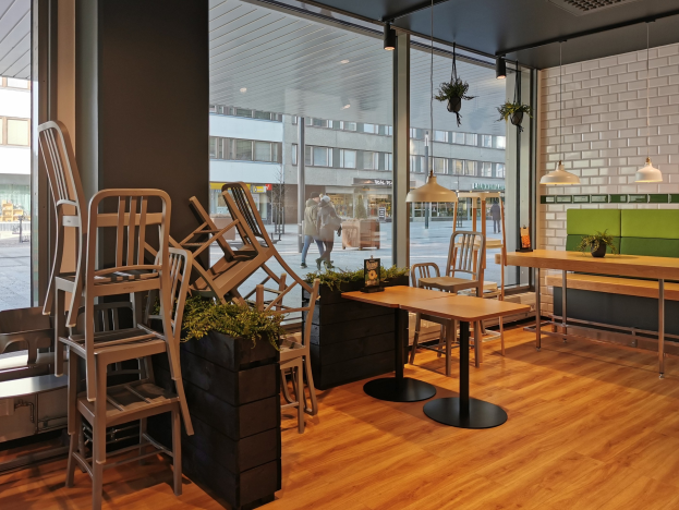 Ein Berliner Restaurant mit hölzernen Tischen und Stühlen in der Nähe eines großen Fensters, das eine Außenansicht von Fußgängern, Gebäuden und Straßenelementen zeigt.