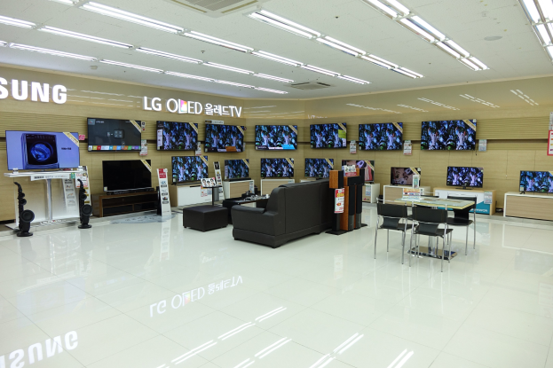 Ein großer, hell erleuchteter Raum mit zahlreichen Fernsehern an den Wänden, begleitet von Sofas, Tischen, Stühlen und anderen Möbeln.