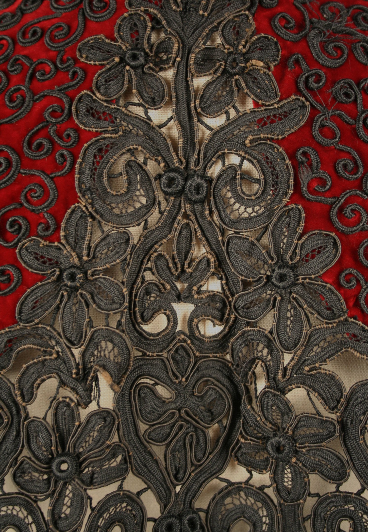 Nahaufnahme eines roten Kleids mit schwarzer Spitzenüberlagerung, das detaillierte Spitzenmuster auf rotem Stoff zeigt.