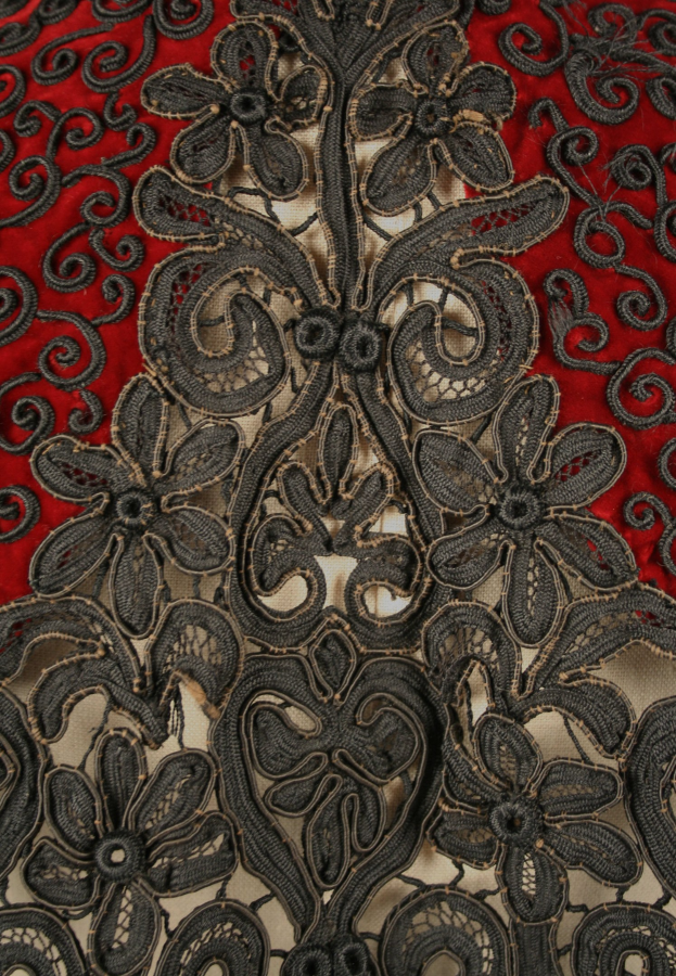 Nahaufnahme eines roten Kleids mit schwarzer Spitzenüberlagerung, das detaillierte Spitzenmuster auf rotem Stoff zeigt.