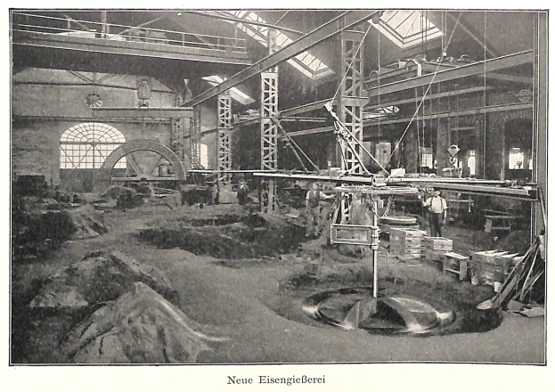 Schwarze und weiße Fotografie einer frühen deutschen Fabrik mit Arbeitern, die Maschinen bedienen, umgeben von Metallstangen und -pfählen, beschriftet mit "Neue Eisenglebeerei, die erste Fabrik in Deutschland" unten.