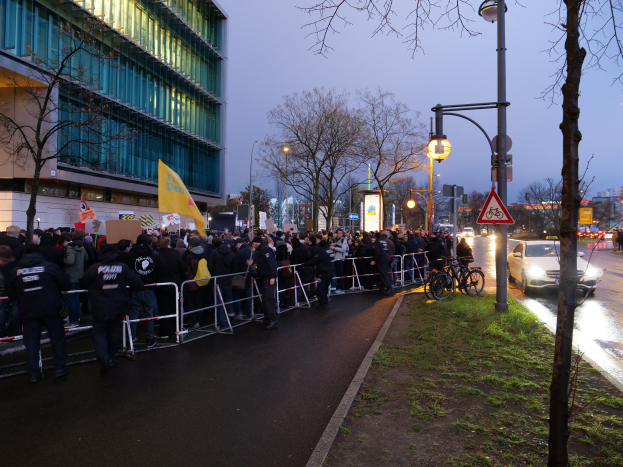 Große Gruppe von Menschen mit Schildern vor einem Gebäude mit Barrikaden, Fahrrädern und Schildern, was auf eine Protestaktion in Berlin hindeutet.