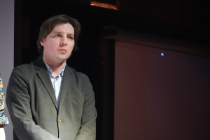 Ein Mann im Anzug und eine Frau stehen Seite an Seite auf einer Bühne und haben beide ernste Gesichter.