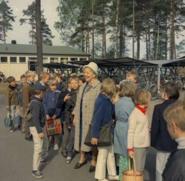 Kinder, die vor einem Gebäude an einer Schule in Schweden in den 1960er Jahren mit Fahrrädern, Schuppen und Bäumen im Hintergrund stehen.
