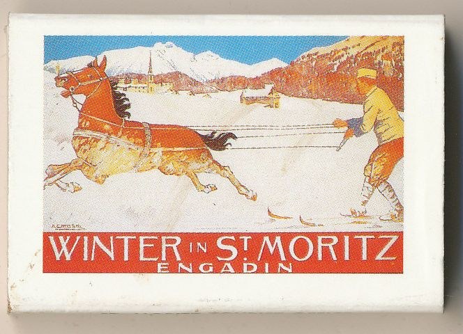 Streichholzschachtel mit einer Illustration eines Pferdes und einer Person, Text "Winter in St. Moritz, Engadin" vor schneebedeckten Bergen und einem klaren blauen Himmel.