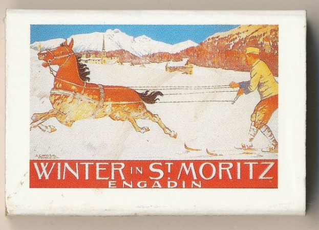 Streichholzschachtel mit einer Illustration eines Pferdes und einer Person, Text "Winter in St. Moritz, Engadin" vor schneebedeckten Bergen und einem klaren blauen Himmel.