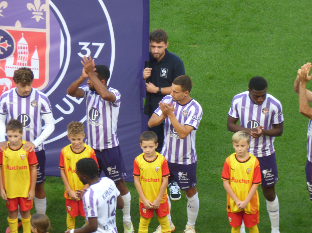 Eine Gruppe junger Jungs steht auf einem grünen Fußballfeld und klatscht in die Hände mit einem Banner und Logos im Hintergrund.