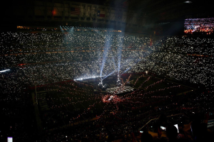 Eine gro├če Menge Menschen in einem Stadion bei Nacht, beleuchtet von hellen Lichtern, mit einem Bildschirm auf der rechten Seite, der wahrscheinlich die Ergebnisse der Super-Bowl-XLVII-Halbzeitshow anzeigt.