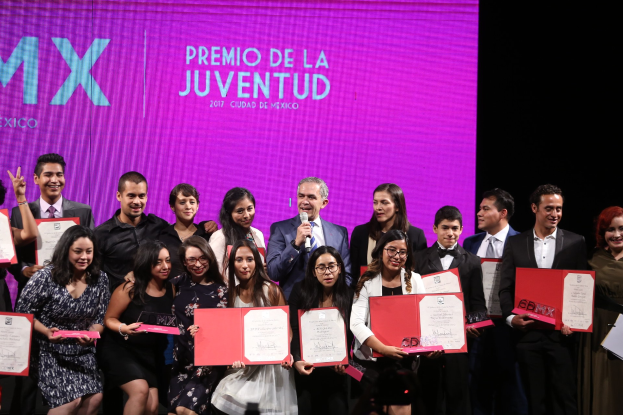 Gruppe von Menschen auf einer Bühne mit Urkunden, Mann spricht in ein Mikrofon und Bildschirm zeigt "Premio de la Juventud 2017" im Hintergrund.