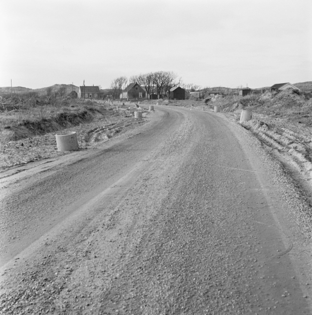 Ein Schotterweg schlängelt sich durch eine ländliche Gegend, gesäumt von Bäumen und Häusern, mit verschiedenen Gegenständen, die entlang des Weges und des Himmels im Hintergrund verstreut sind.