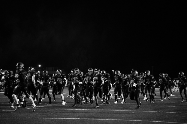 Schwarzes und weißes Bild von Fußballspielern in Helmen, die nachts auf das Feld laufen, umgeben von Stadionlichtern und Pfählen.