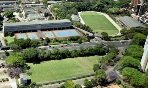 Luftaufnahme eines Fußballfeldes an der Universität Sydney, umgeben von Bäumen, Gebäuden und Fahrzeugen, mit einer neuen Sportanlage in Planung.