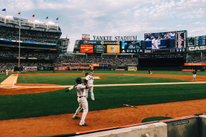 Baseballspiel im Yankee Stadium mit Spielern, Zuschauern, Stadionwerbung und einem bewölkten Himmel.