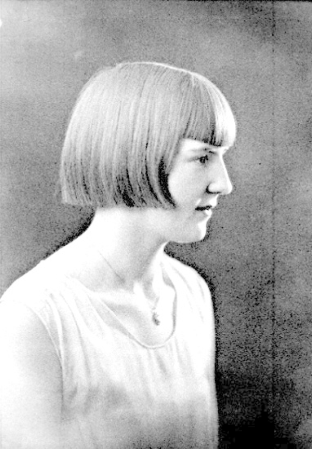Ein Schwarz-Weiß-Foto einer Frau mit einem kurzen Bob-Haarschnitt, ihr Gesicht ist zu sehen, die Augen schauen zur Seite und die Lippen sind leicht geöffnet.