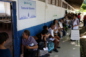 Eine Gruppe von Menschen, die auf Bänken vor einem Gebäude mit einer Tafel und einer Tür sitzen und in einer Schlange vor einer Wahllokal in Guadalajara, Mexiko, warten.