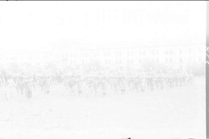 Schwarzes und weißes Foto von Radrennfahrern im Schnee mit einem Gebäude im Hintergrund.