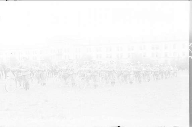 Schwarzes und weißes Foto von Radrennfahrern im Schnee mit einem Gebäude im Hintergrund.