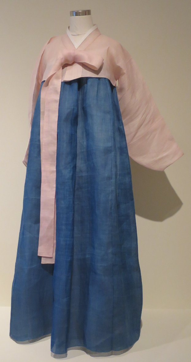 Eine Schaufensterpuppe in einem blauen und pinkfarbenen Hanbok mit komplexen Mustern auf einem neutralen Hintergrund in einem Museum.