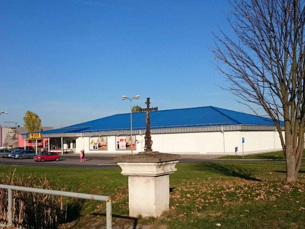 Ein großes Gebäude mit einem blauen Dach, das als St. Paul's Catholic Church identifiziert wurde, umgeben von einem Metallzaun, Gras, trockenen Blättern, Bäumen, Fahrzeugen, Menschen auf einem Fußweg, Polen, Schildern, einer Fahne mit Text, anderen Gebäuden mit Fenstern und einem bewölkten Himmel.
