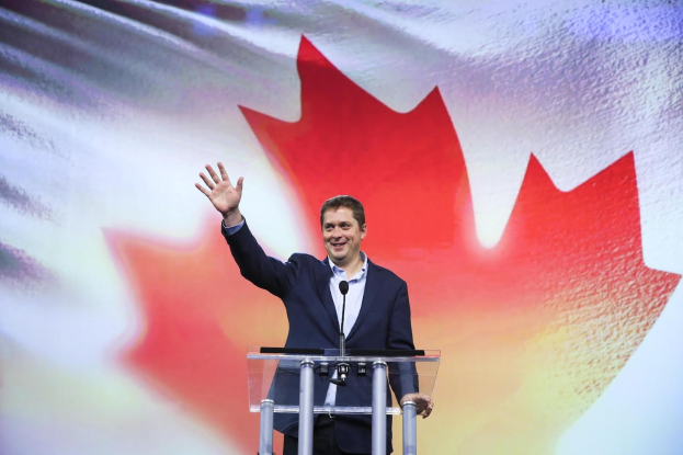 Der kanadische Premierminister Alex Salmond steht an einem Podium mit Mikrofonen, lächelt vor einer kanadischen Flagge, mit einem Bildschirm im Hintergrund.