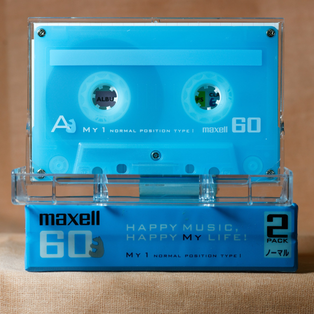 Eine blaue Kassette mit der Aufschrift "Maxell Happy Music, Happy My Life", die auf einer braunen Oberfläche steht.