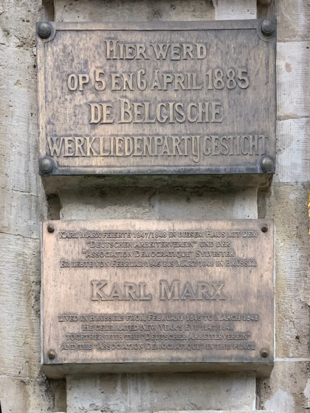 Metallplatte an einer Gebäudewand mit "Karl Marx" in fetter schwarzer Schrift.