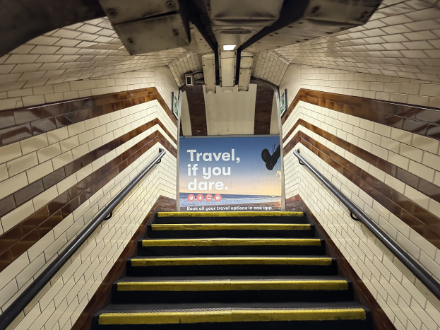 Eine Treppe in einer U-Bahn-Station mit einem Schild, das 'Reise, wenn du wagst' trägt, flankiert von Geländern auf beiden Seiten.