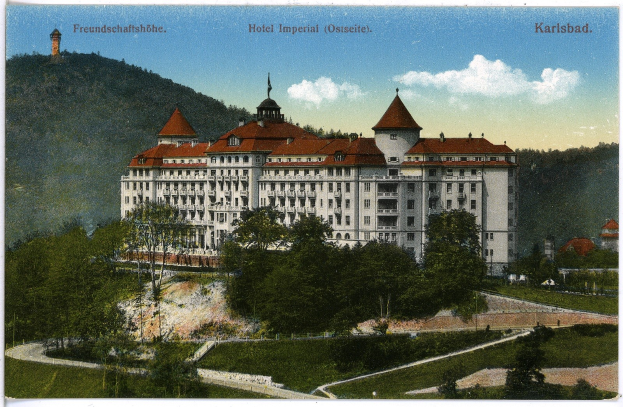 Alte Ansichtskarte des Hotel Imperial in Karlsbad, Deutschland, zeigt ein großes Gebäude mit Fenstern umgeben von Bäumen, Pflanzen, Gras, einem Pfad, einer Baumgruppe, Hügeln und einem bewölkten Himmel, mit Text oben.