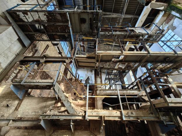 Altes industrielles Gebäude mit einem zentralen Metallrahmen, umgeben von verrosteten Eisenstäben, Treppen, Wänden und Fenstern, zeigt Anzeichen von Verfall und Verfall.