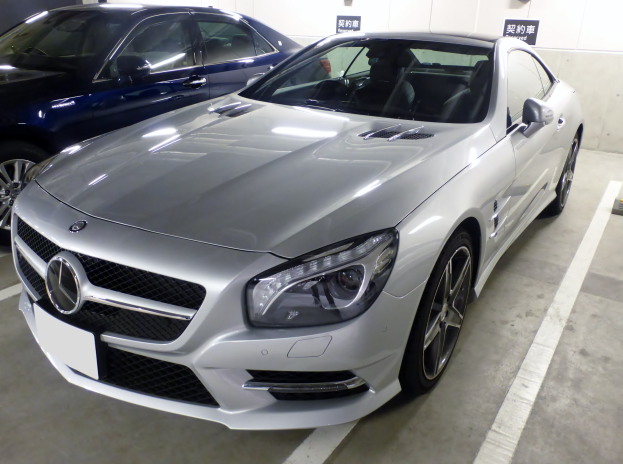 Ein silberner Mercedes-Benz SL-Class in einer Garage neben anderen Autos geparkt, mit Texttafeln im Hintergrund.