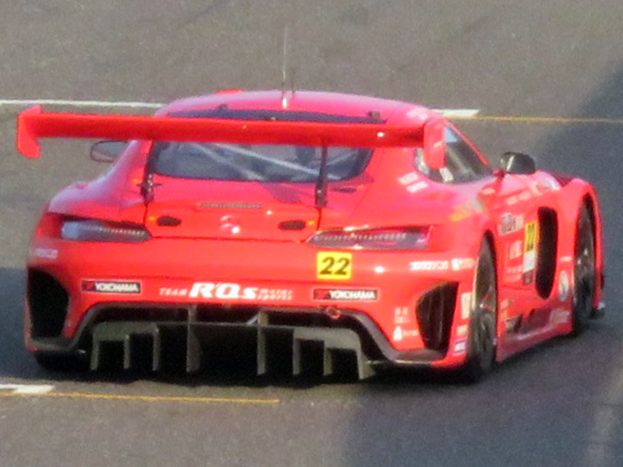 Roter Porsche 911 GTS Rennauto auf einer Rennstrecke mit aerodynamischem Design, großem Heckflügel, breiter Standfläche und schwarzen Rädern.