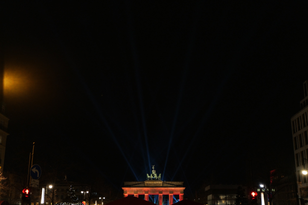 Brandenburger Tor in Berlin nachts, beleuchtet von Straßenlaternen, mit umliegenden Gebäuden, Bäumen, Pfählen, Verkehrszeichen, Schildern und Zelten unter einem dunklen Himmel.