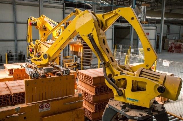 Industrielager mit gestapelten Kisten, Kränen, Zaun, Pfählen und einer fernen Wand in einer Fertigungsanlage.