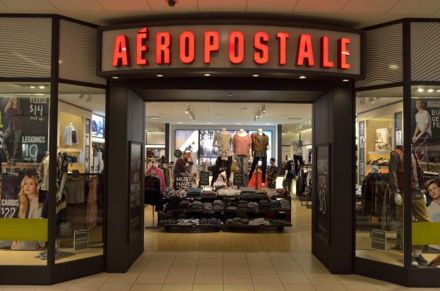 Innenansicht eines Aeropostale-Ladens in einem Einkaufszentrum mit Kleiderstangen, Schaufensterpuppen in Kleidern, Texttafeln, Glaswänden und Beleuchtung sowie einer Ankündigung zum Schließen im Juni.