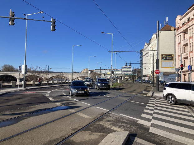 Stadtstraße mit fahrenden Autos, eine Zebrastreifen, Laternen, Ampeln, Schilder, Gebäude mit Fenstern, Bäume, eine Brücke und einen Himmel als Hintergrund.