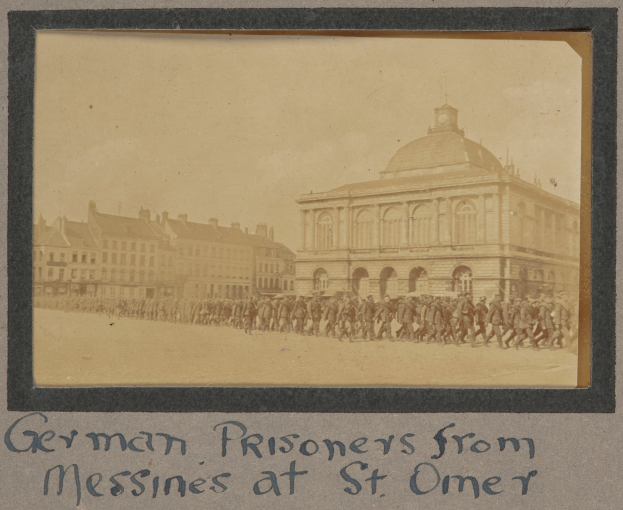 Deutsche Kriegsgefangene aus Messines vor einem Gebäude mit Text unten unter einem klaren blauen Himmel.