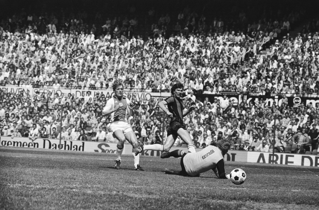Schwarzes Foto von Männern, die auf einem Feld Füßball spielen, mit Zuschauern im Hintergrund und einer Tafel mit der Aufschrift "Bundesliga 1978-79 Ajax 1-1 Hannover 96."