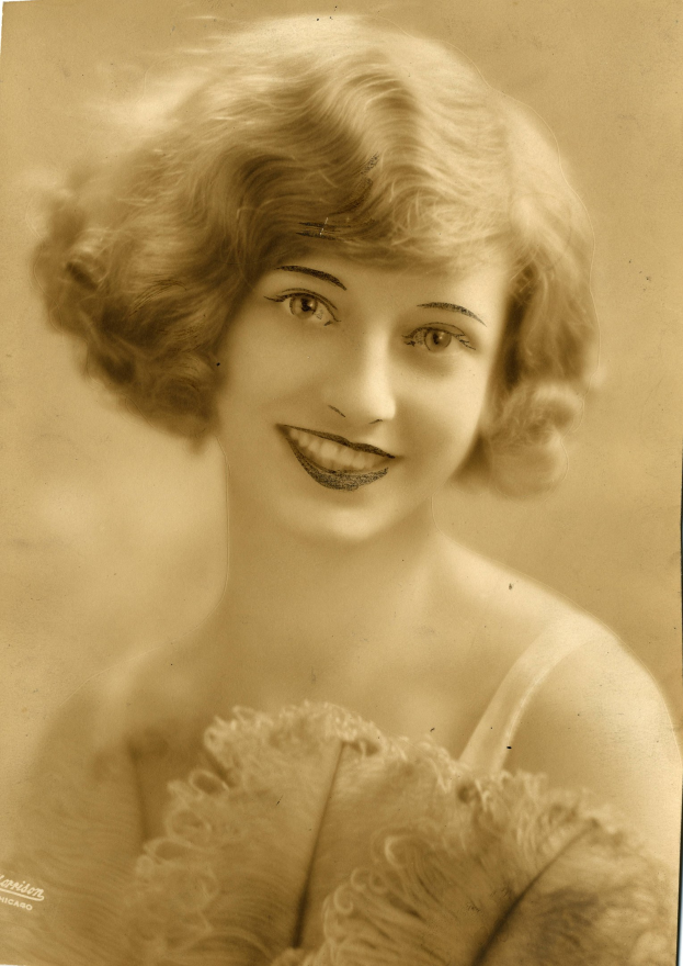 Ein Schwarz-Weiß-Foto einer älteren Frau in einem Kleid mit einer 1920er-Frisur, die warm lächelt.