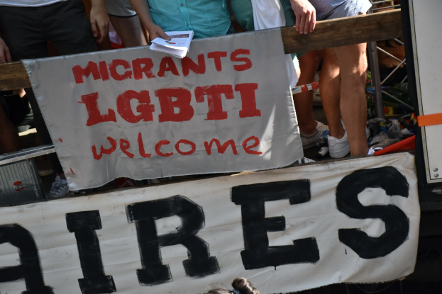 Gruppe von Menschen mit einem Schild, auf dem "Migranten LGBT Willkommen Aires" steht, und einer Decke sowie verstreuten Schuhen in der Nähe.