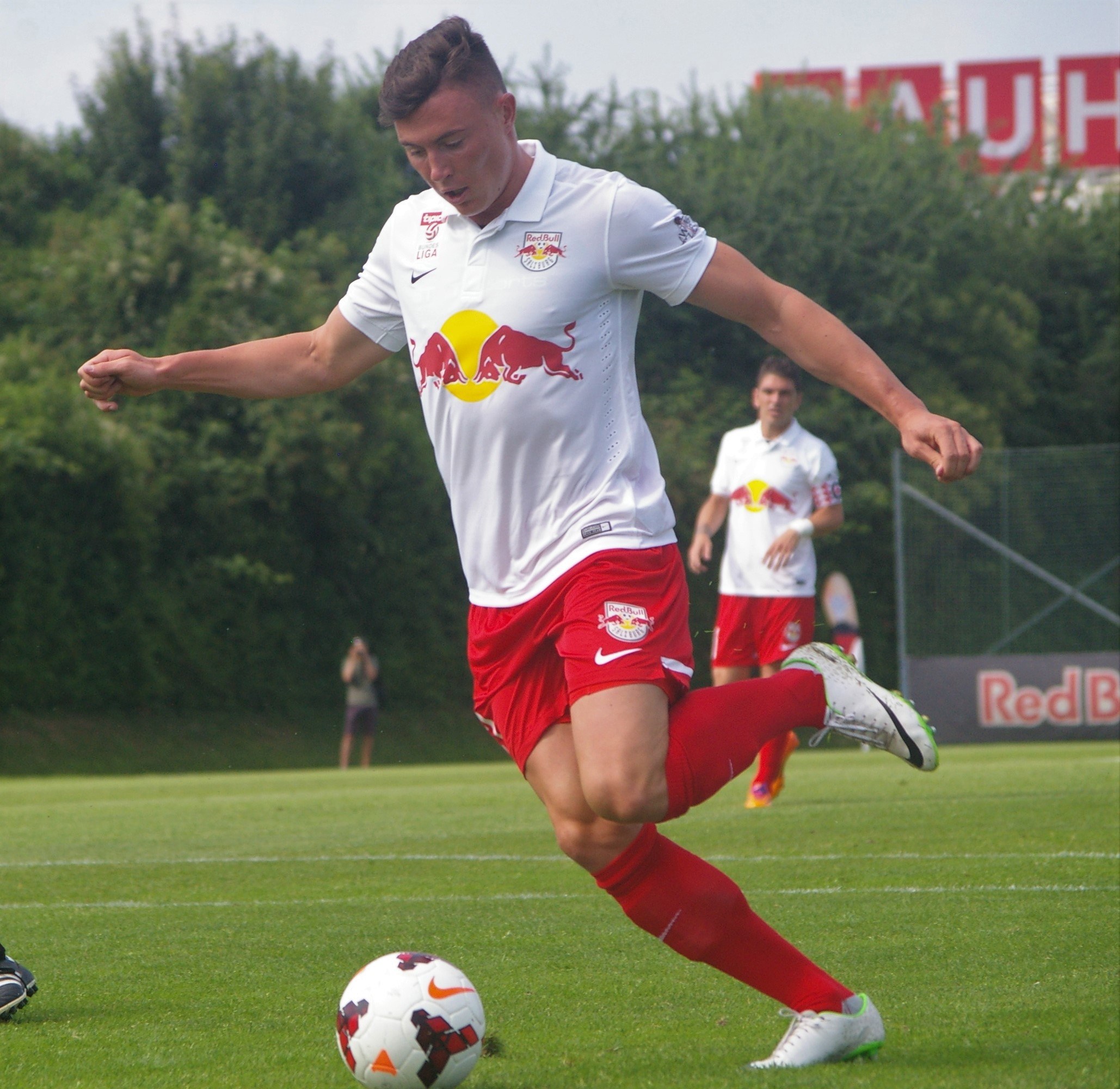 Ein professioneller Fußballspieler, der einen Ball auf einem Rasenfeld kickt, mit 'RB Leipzig' im Hintergrund.