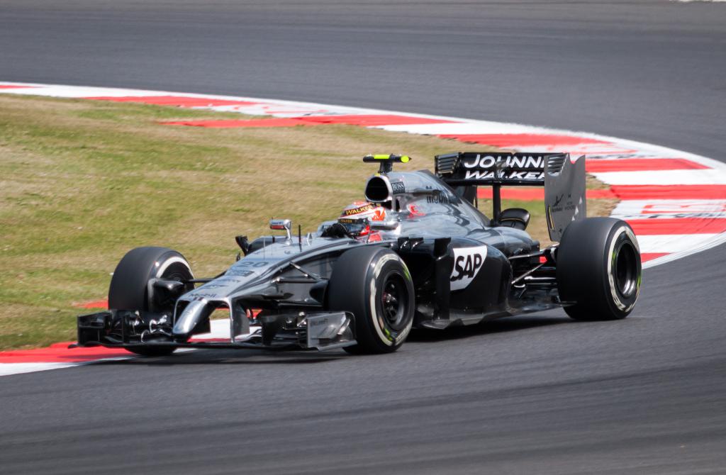 Ein Rennwagen fährt auf einer leeren Straße mit Grasfläche im Hintergrund.